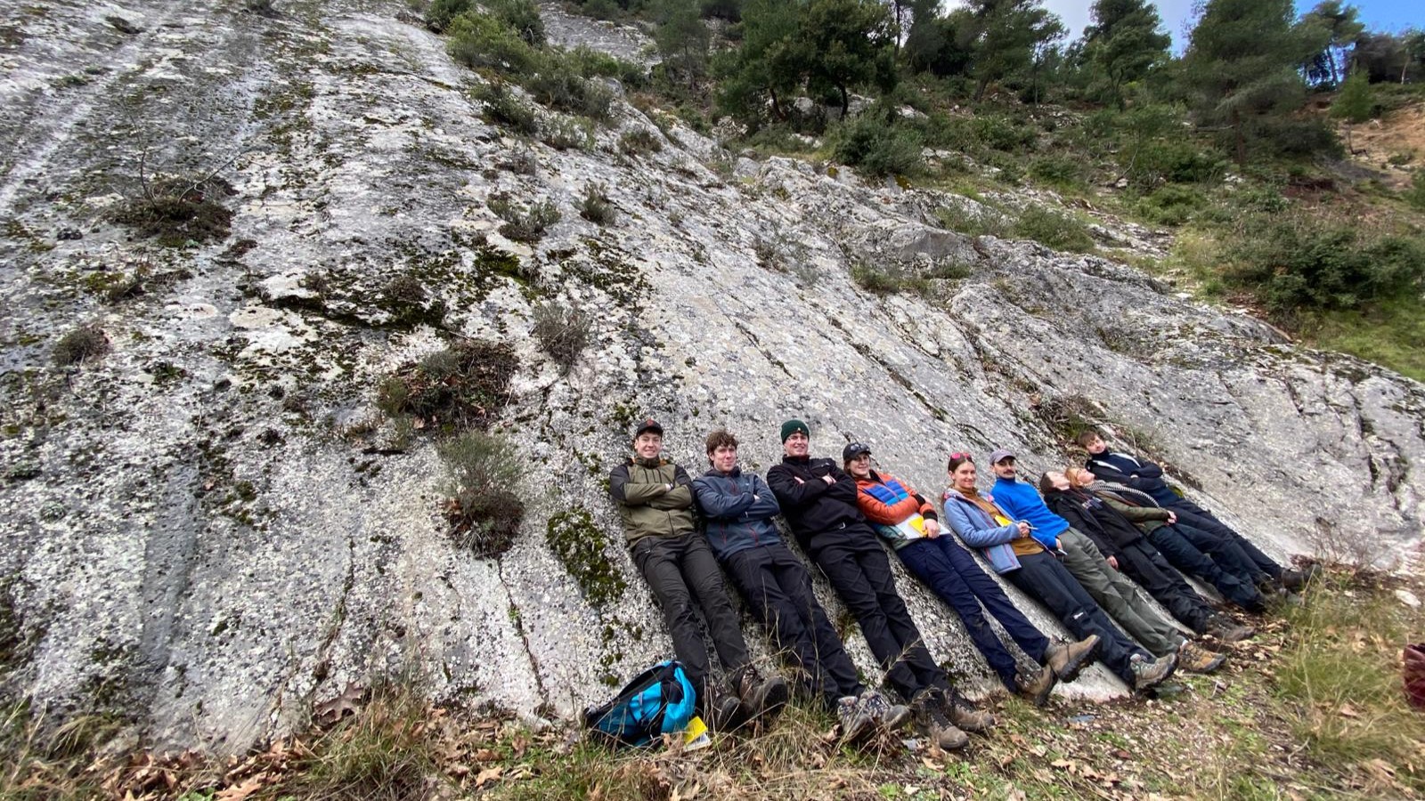 A group of people lying next to each other at the foot of a rock formation